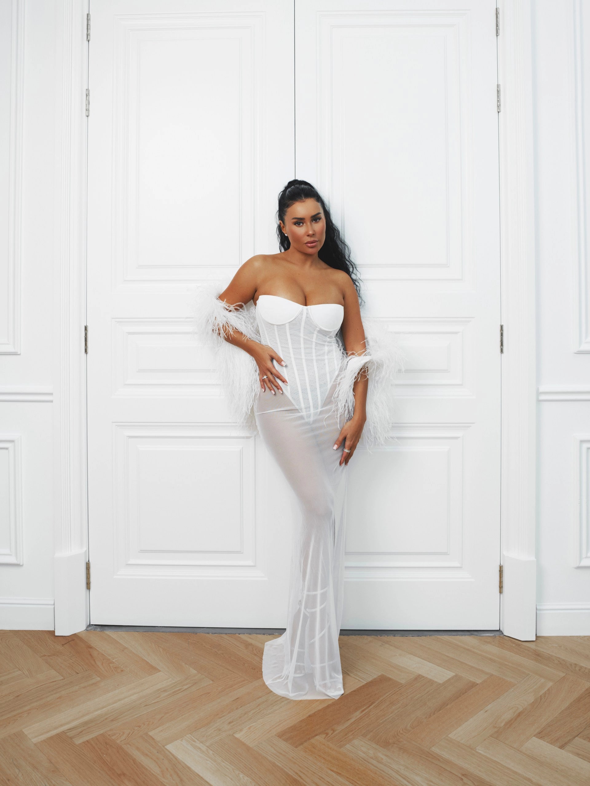 Woman in a white strapless gown standing against a white paneled wall.