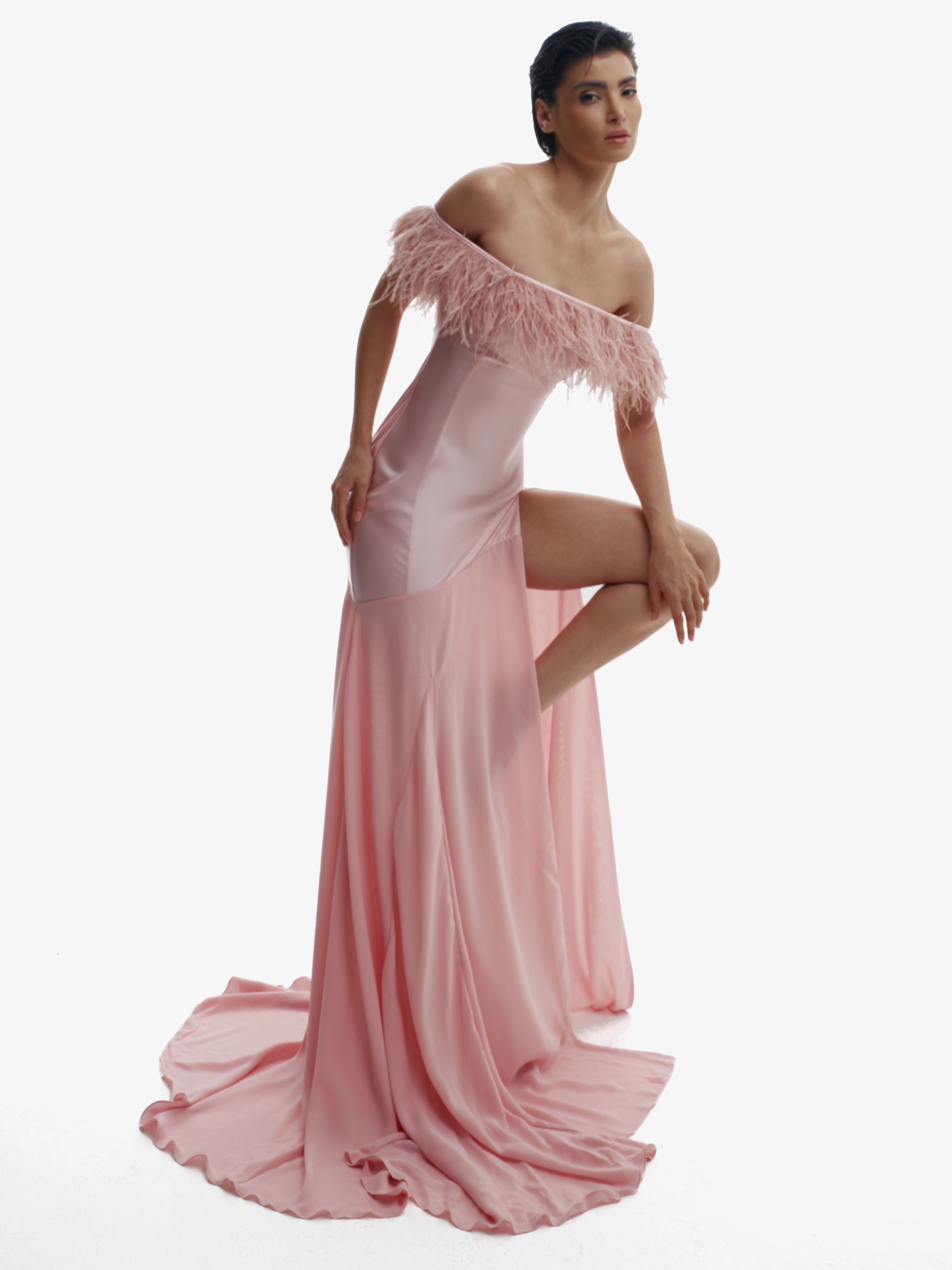 Woman wearing a pink off-shoulder gown with fringe details on a white background
