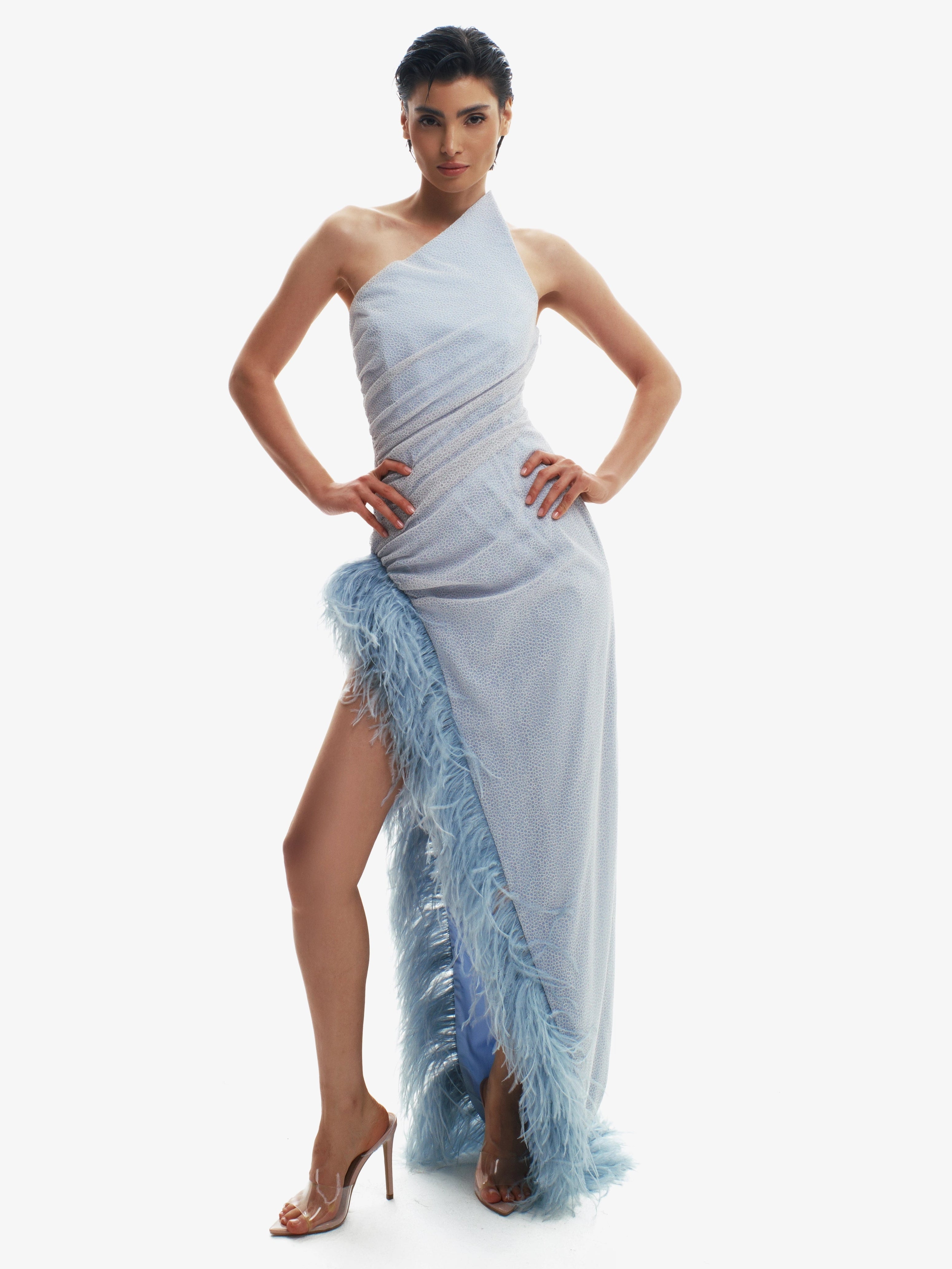 Woman wearing a light blue one-shoulder dress with a slit on a white background