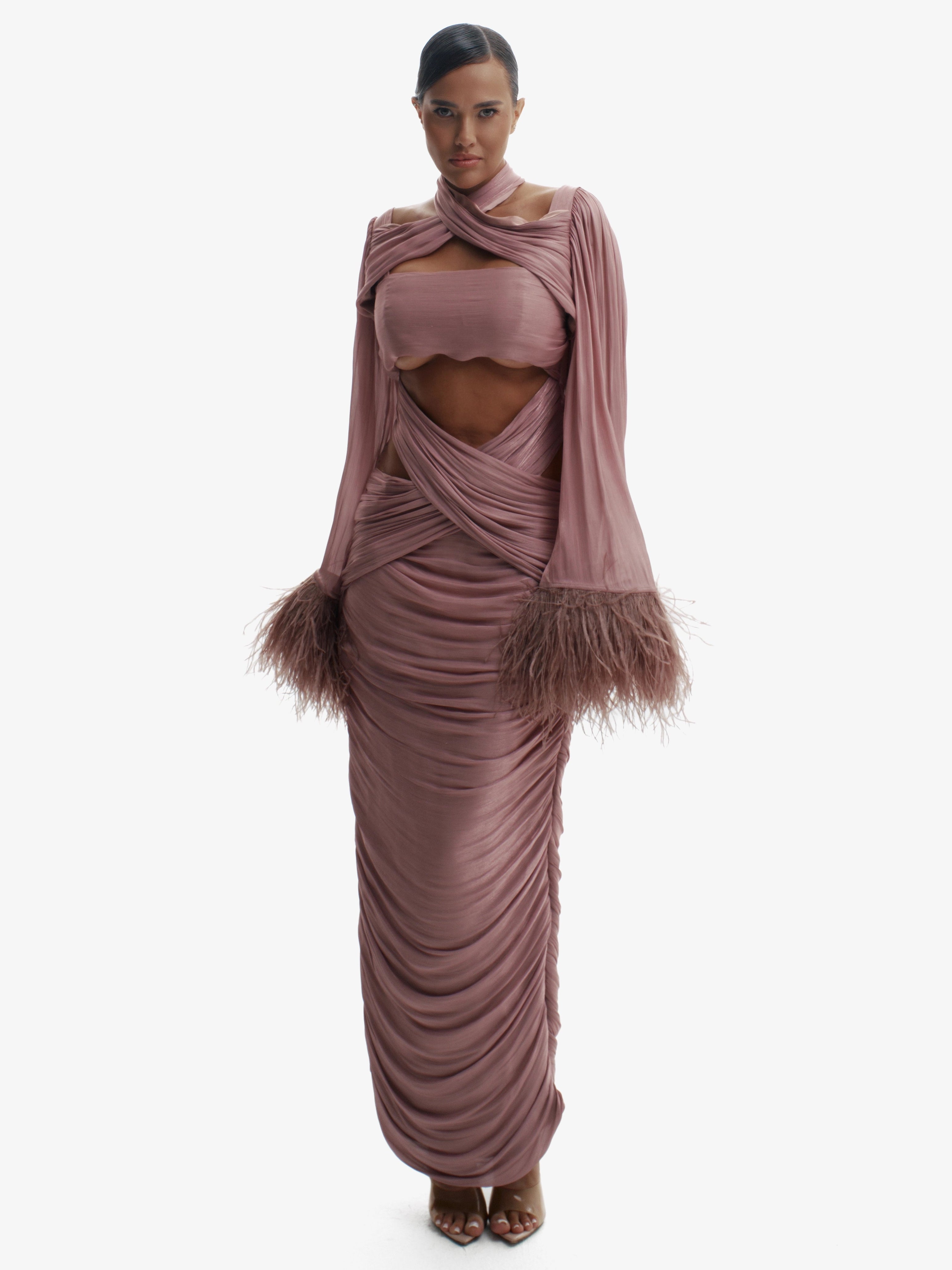 Woman wearing a long, flowing dress with feathered details on a white background