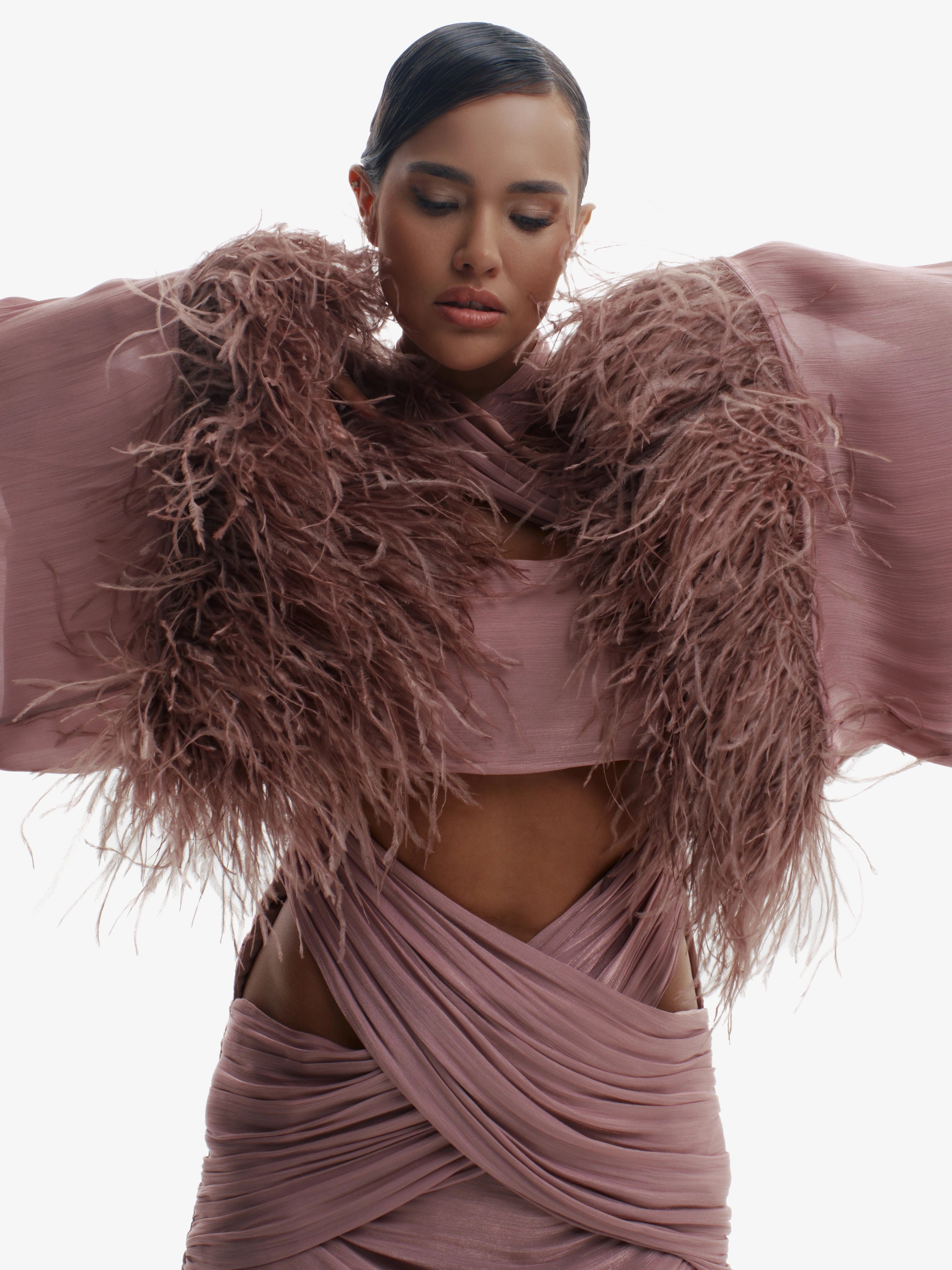 Woman wearing a mauve outfit with feathered sleeves against a white background