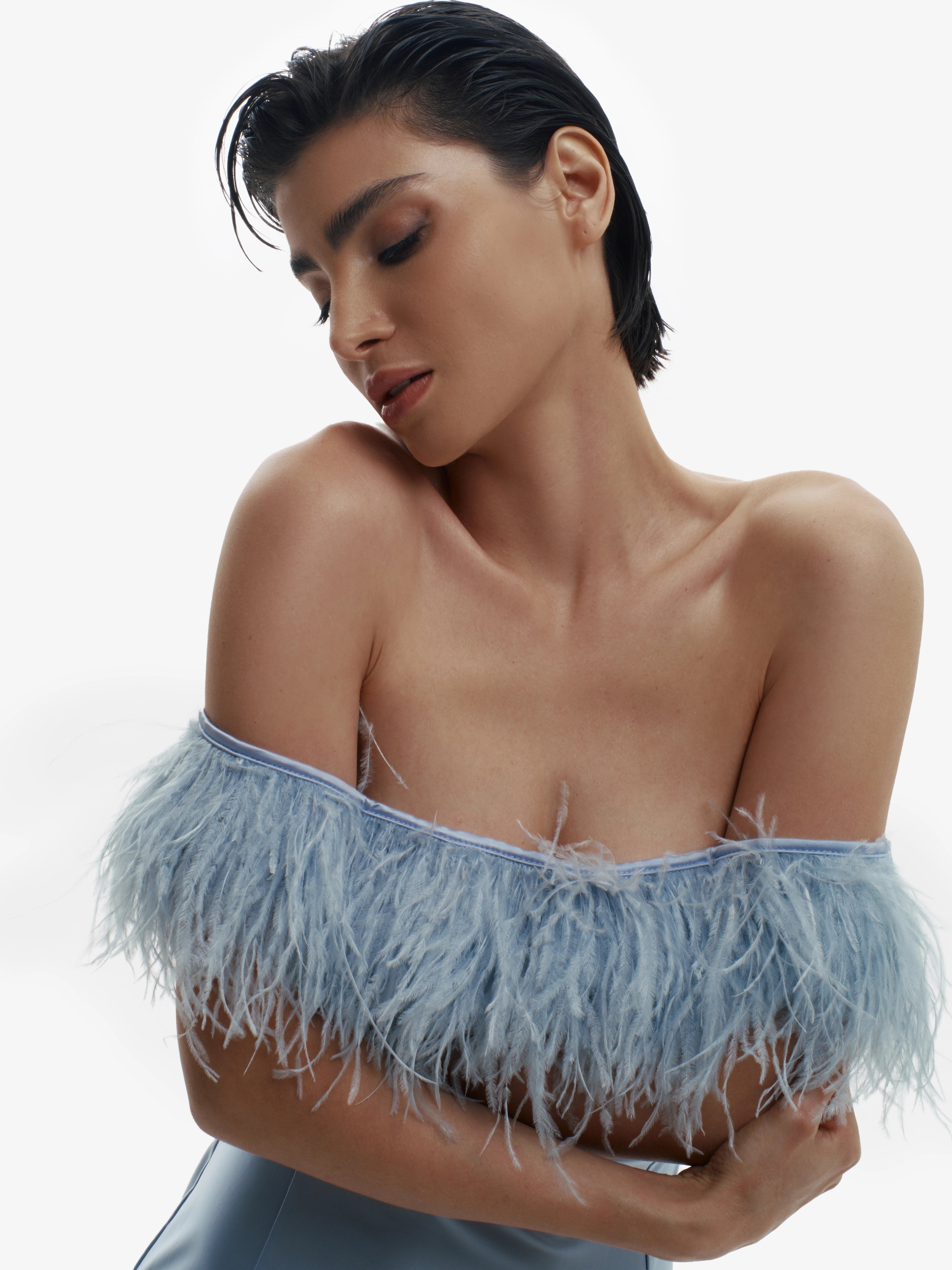 Woman wearing a light blue off-shoulder top with feather details on a white background
