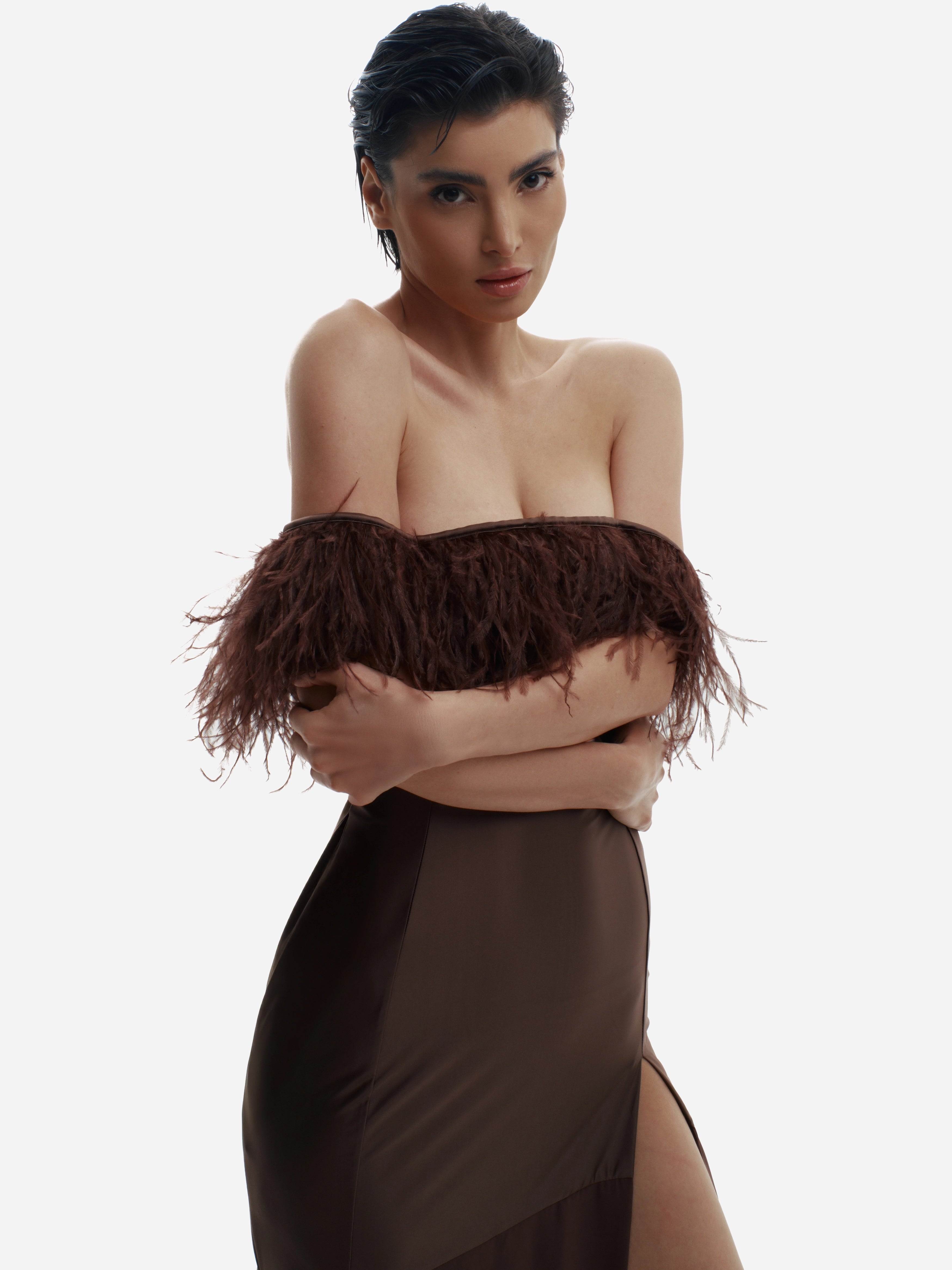 Woman wearing a brown off-shoulder top with feather details and a matching skirt on a white background